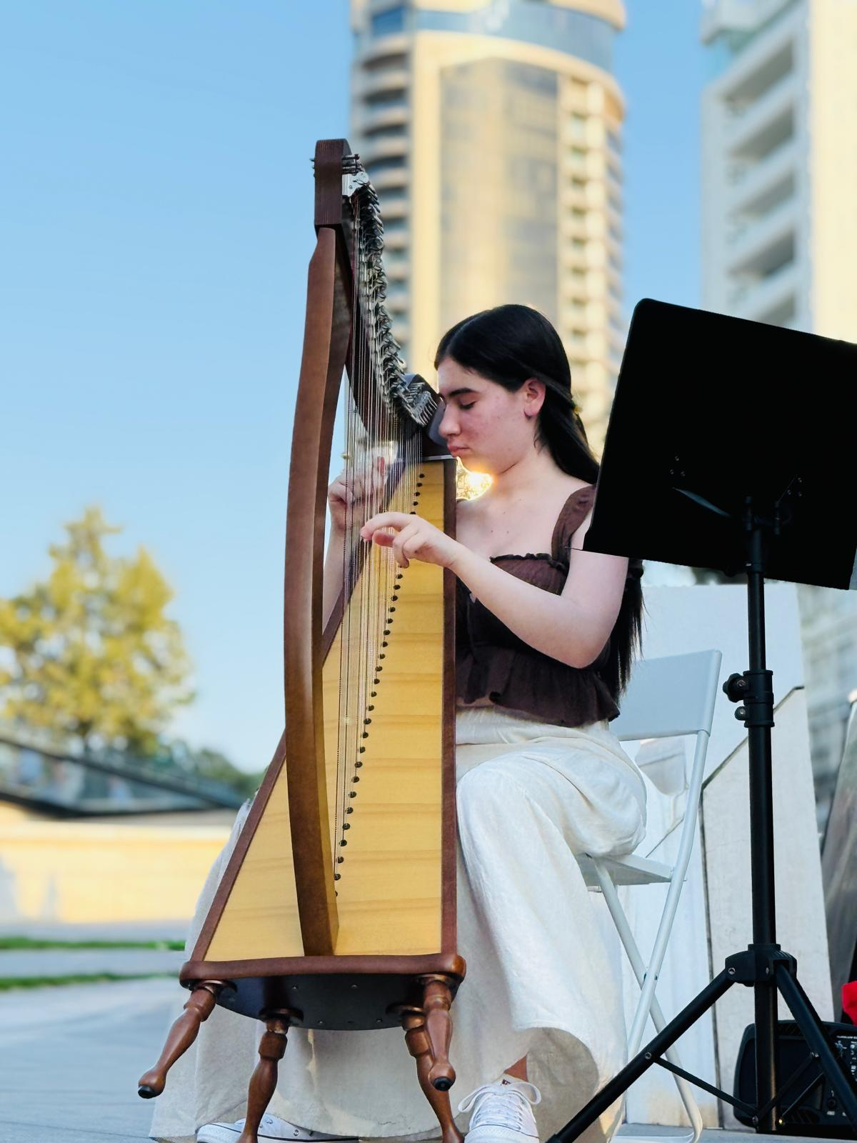 Angelina playing a solo harp performance outdoors in daylight